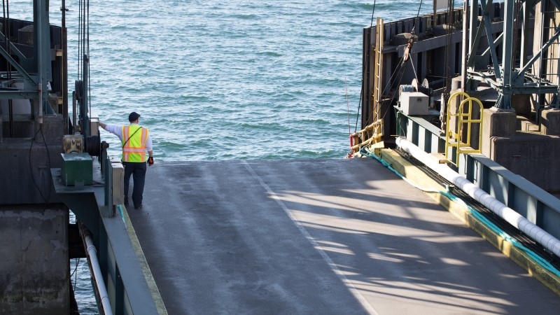 Longshore dock worker in a reflective vest, at the edge of a ferry boat pier, with water in the background